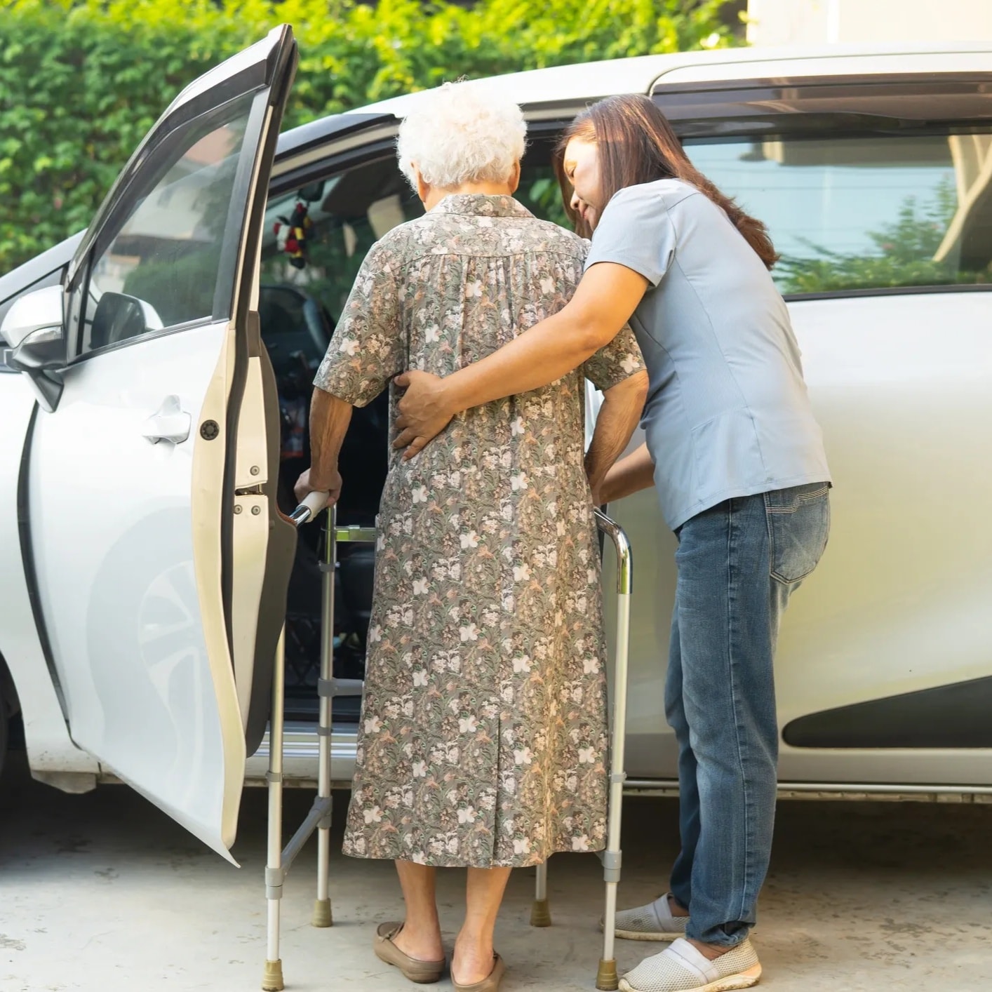 Caregiver helping an older adult into a passenger vehicle — car door open, both people and the vehicle clearly visible